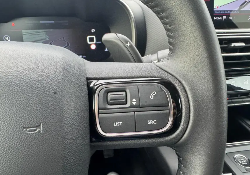Gros plan sur les commandes au volant du Citroën C5 Aircross 2024 hybride, avec tableau de bord numérique en arrière-plan.