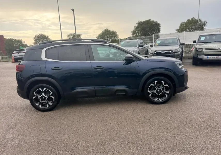 Vue de profil côté gauche d’un Citroën C5 Aircross hybride bleu foncé avec barres de toit et jantes alliage 18 pouces.