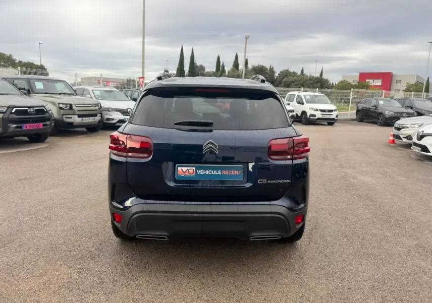Vue arrière d'un Citroën C5 Aircross hybride bleu foncé, avec barres de toit et feux arrière LED visibles, sur parking extérieur.