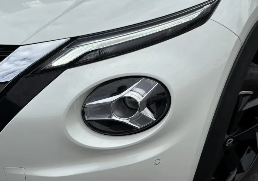 Gros plan sur le phare antibrouillard avant droit du Nissan Juke blanc perle, soulignant ses lignes modernes et la calandre noire.