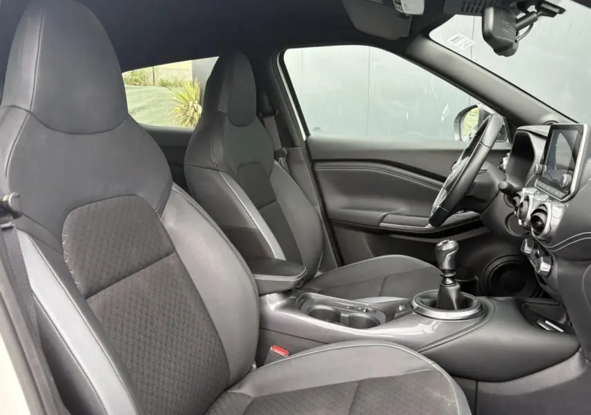 Intérieur noir et gris du Nissan Juke 2023, vue côté gauche montrant sièges, volant et levier de vitesse manuel.