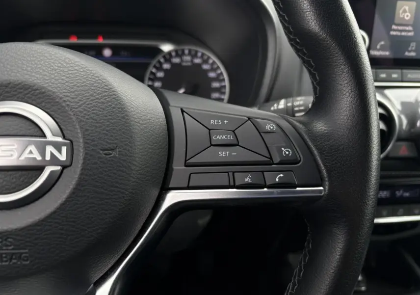 Gros plan sur le volant noir du Nissan Juke 2023, côté droit, avec commandes de régulateur de vitesse et téléphone.