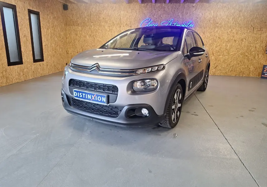 Citroën C3 gris en 3/4 avant droit, avec jantes aluminium et détails noirs sur les rétroviseurs et bas de caisse.