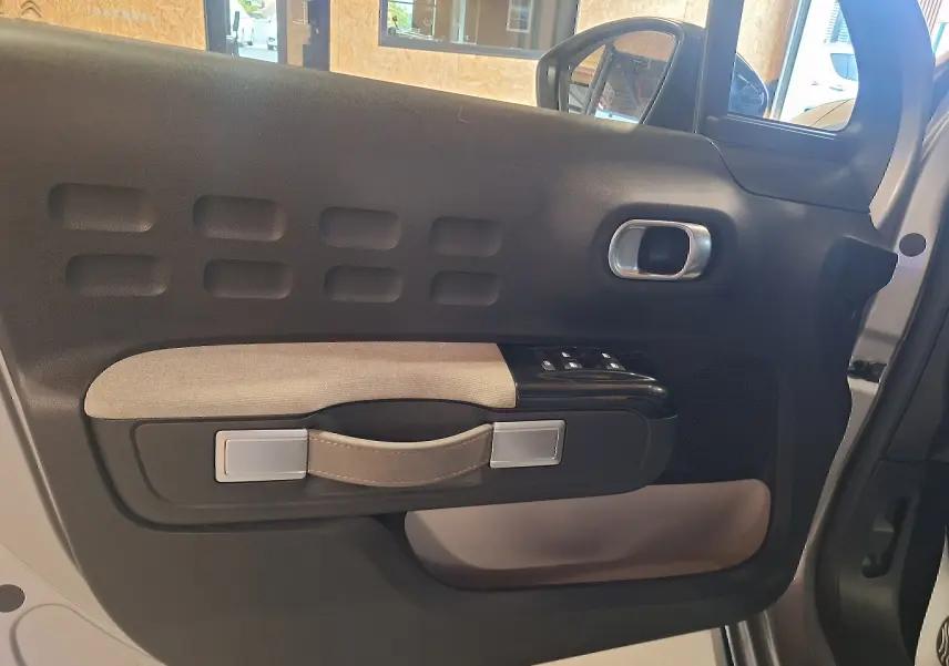 Vue intérieure côté gauche de la porte avant grise de la Citroën C3 avec poignée en tissu beige et commandes de vitres.