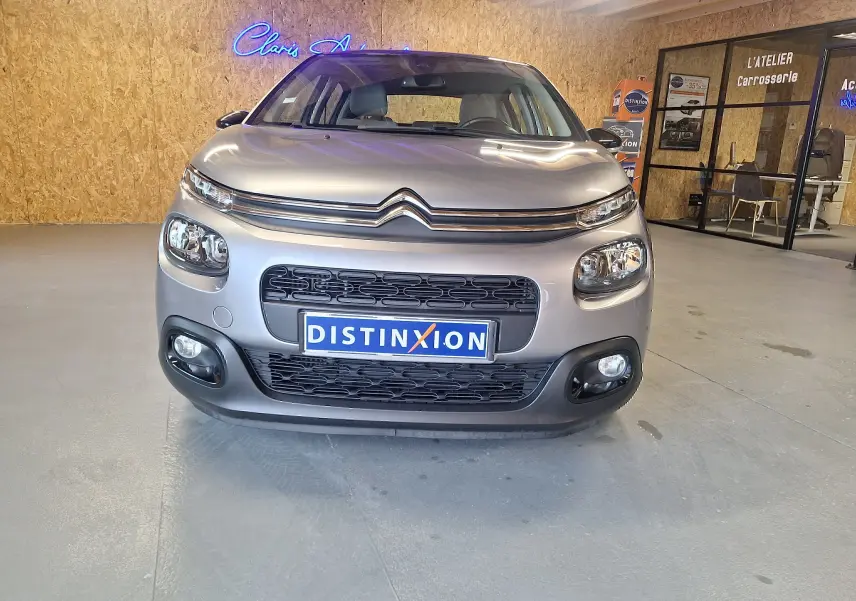 Vue de face d'une Citroën C3 gris métallisé avec calandre noire et phares arrondis dans un garage.