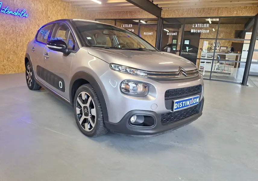 Citroën C3 gris 3/4 avant droit en intérieur avec protections latérales noires et jantes alu distinctives.