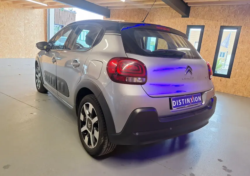 Vue 3/4 arrière droite d'une Citroën C3 gris avec toit noir et jantes alliage dans un garage lumineux.