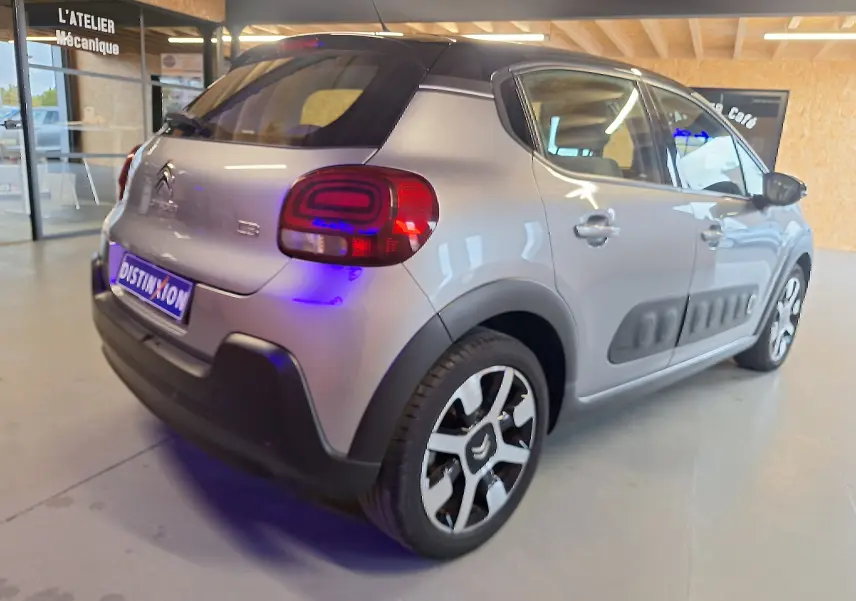 Vue 3/4 arrière droite d'une Citroën C3 gris avec jantes alu et protections latérales noires en intérieur showroom.