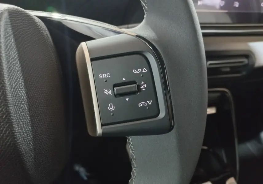 Gros plan sur les commandes gauche du volant cuir gris du Citroën C3 hybride 2025, avec boutons multifonctions visibles.