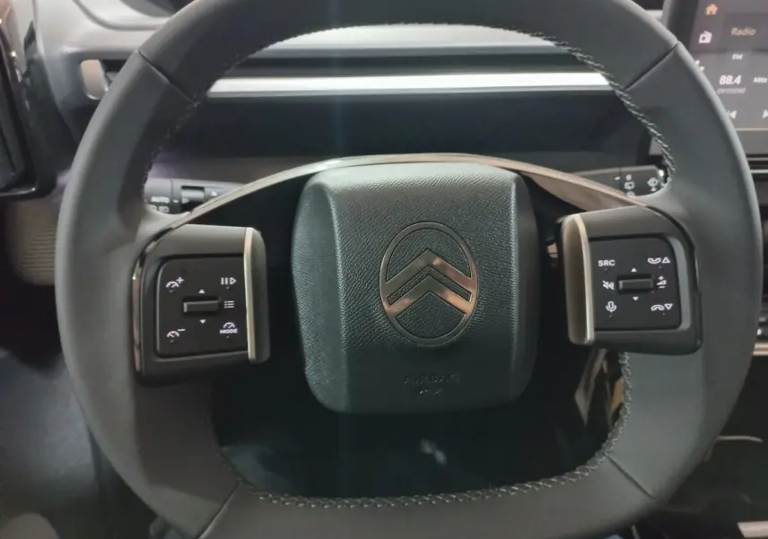 Vue rapprochée du volant cuir noir de la Citroën C3 hybride 2025 avec commandes multifonctions intégrées.