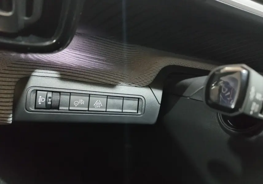 Gros plan sur les commandes de réglage des phares et aides à la conduite dans une Citroën C3 hybride gris foncé, côté conducteur.