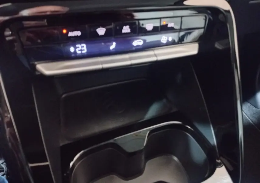 Vue rapprochée de la console centrale noire de la Citroën C3 hybride 2025 avec commandes climatisation et zone de recharge par induction.