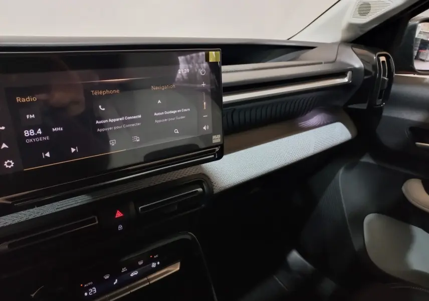 Vue intérieure côté passager du tableau de bord de la Citroën C3 hybride 2025 avec écran tactile et garniture gris clair.