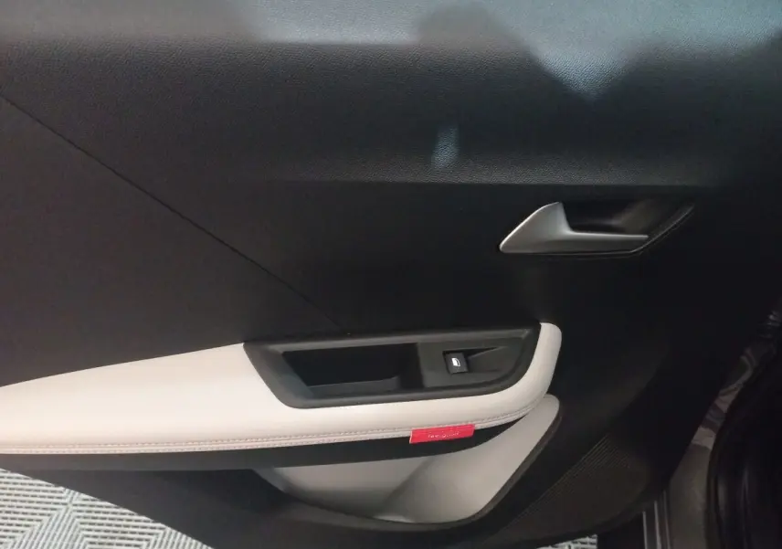 Vue intérieure côté gauche de la porte d'une Citroën C3 hybride 2025 avec garniture noire et beige et bouton de verrouillage.