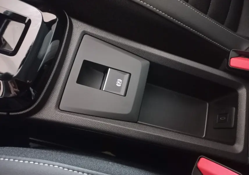 Gros plan sur la console centrale noire de la Citroën C3 hybride 2025, avec frein à main électrique et port USB visible.
