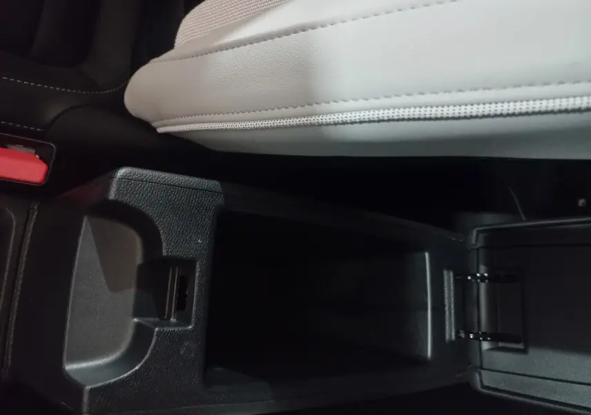 Vue rapprochée de la console centrale ouverte de la Citroën C3 hybride 2025, avec accoudoir gris clair et compartiment noir.