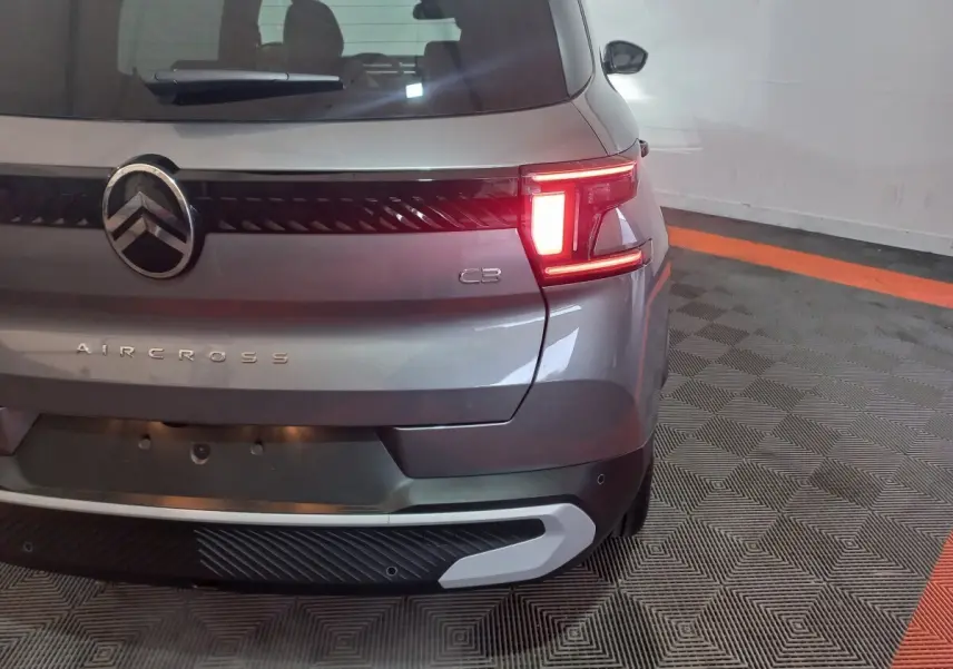 Vue arrière droite d'une Citroën C3 Aircross gris foncé avec feu arrière allumé et logo visible.