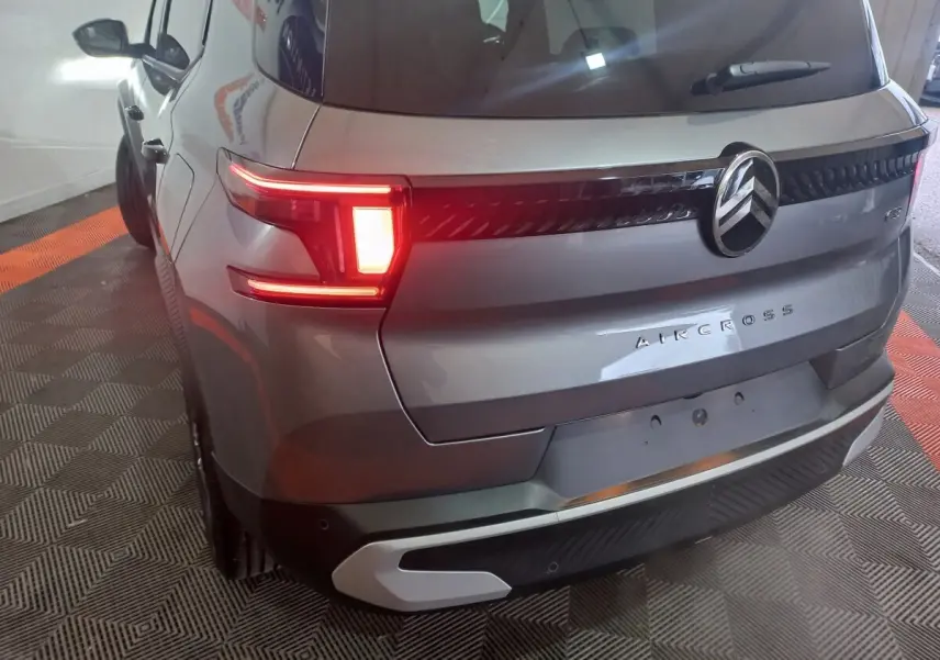 Vue 3/4 arrière gauche d'un Citroën Aircross gris foncé avec feux arrière allumés et logo central chromé.