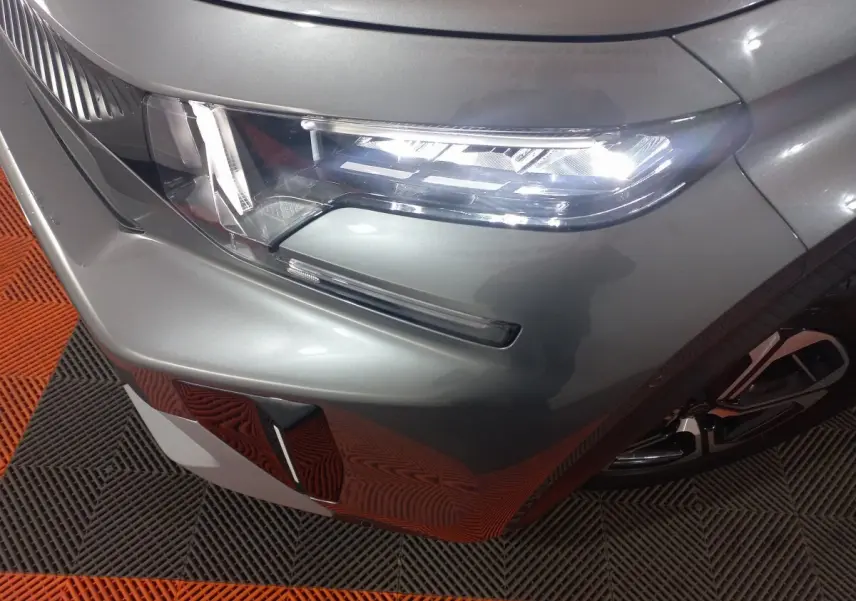 Gros plan sur le phare avant droit d'une Citroën C3 hybride 2025 gris foncé avec détail du pare-chocs et jante.