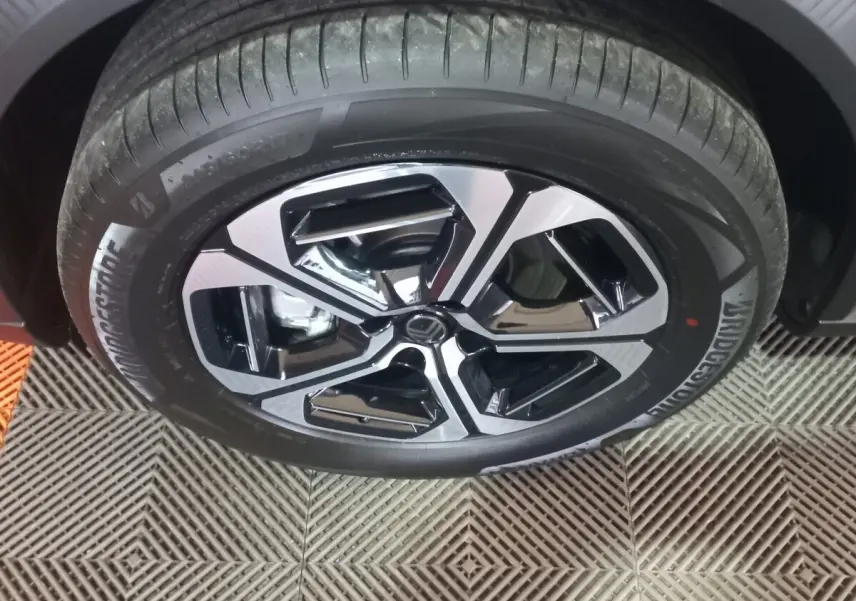 Gros plan sur la jante noire et argentée d’une Citroën C3 hybride gris foncé, avec pneu Bridgestone visible.