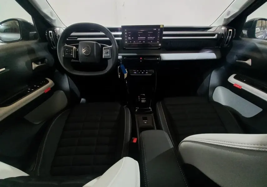 Vue intérieure avant de la Citroën C3 hybride 2025, tableau de bord noir avec écran tactile central et sièges bicolores.