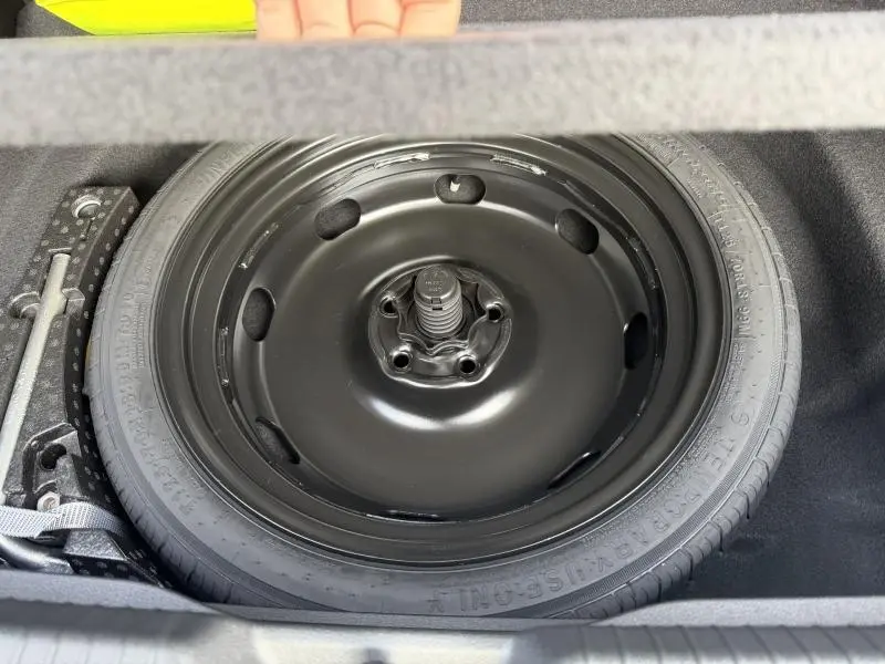 Gros plan sur la roue de secours noire dans le coffre d'une Volkswagen Golf 2025 gris, version hybride essence.