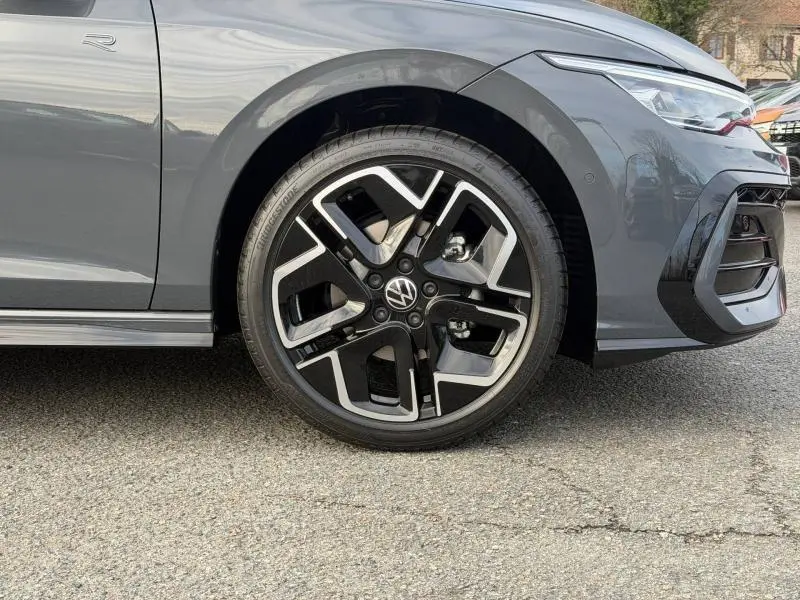 Gros plan sur la roue avant gauche et la partie avant grise d'une Volkswagen Golf 1.5 eTSI R-Line 2025 avec jante noire et argent.
