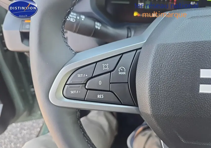 Gros plan sur les commandes multifonctions à gauche du volant du Dacia Duster vert kaki 2025, intérieur visible.