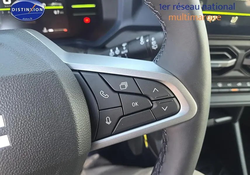 Gros plan sur les commandes au volant multifonction du Dacia Duster 2025, intérieur noir avec écran tactile en arrière-plan.