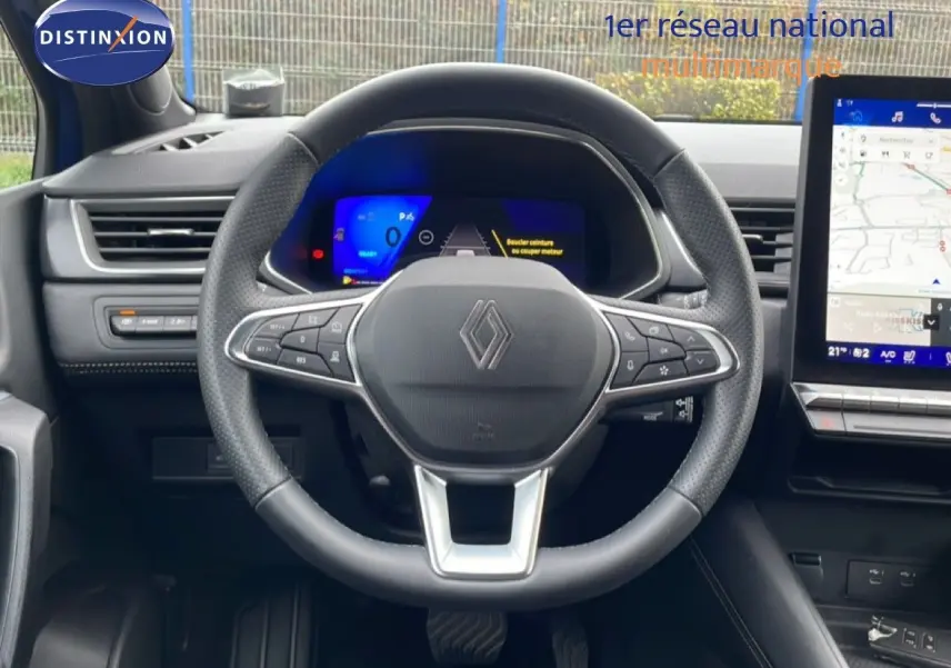 Vue intérieure centrée sur le volant Renault avec tableau de bord numérique et écran tactile de navigation.