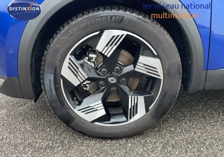 Gros plan sur la roue avant droite d'une Renault Symbioz bleu iron metal avec jante alliage bicolore moderne.