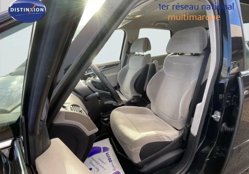Vue intérieure côté conducteur d'une Citroën C4 Picasso noire métal de 2008, sièges tissu beige clair et volant cuir.