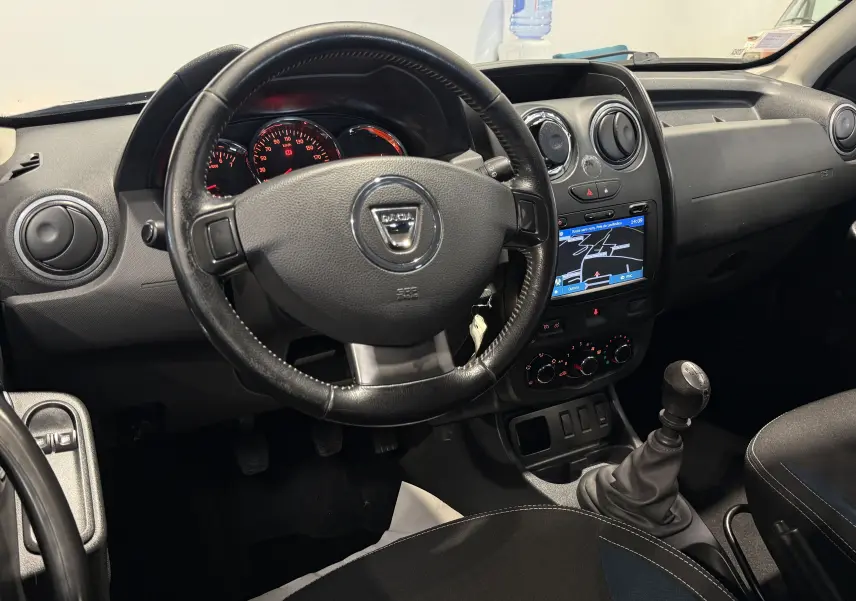 Vue intérieure du tableau de bord du Dacia Duster 2015, avec volant noir, écran tactile et levier de vitesse manuel.