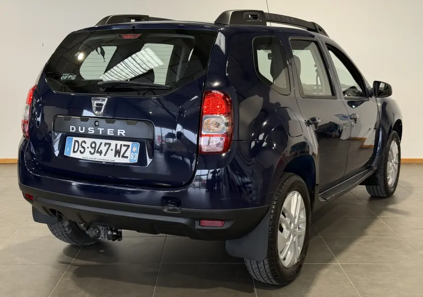 Vue 3/4 arrière droite du Dacia Duster bleu 2015 avec attelage et plaques françaises visibles.