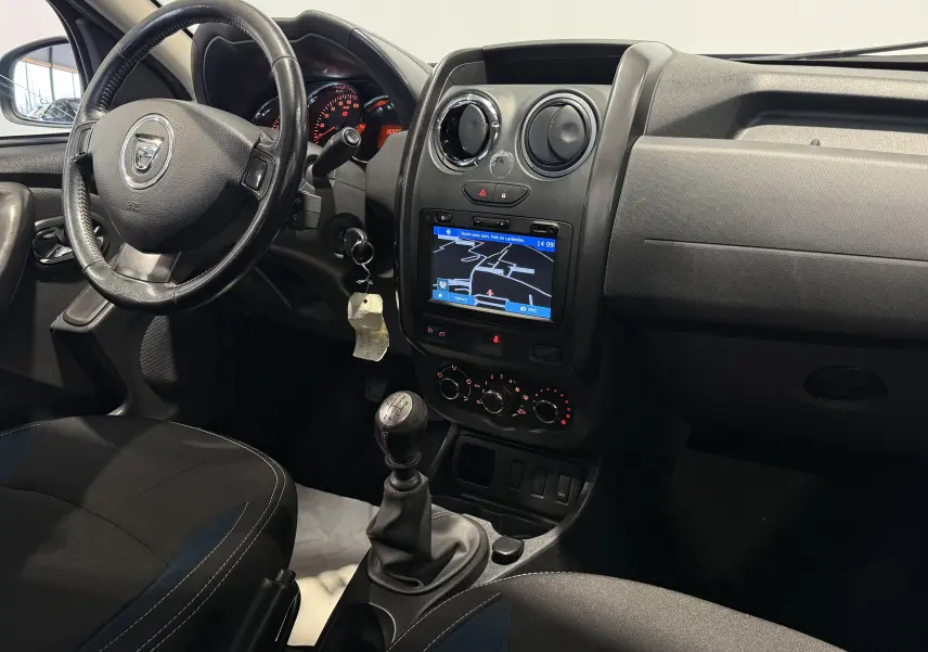 Vue intérieure côté conducteur du Dacia Duster 2015 bleu, montrant le volant, la boîte manuelle et l'écran de navigation.