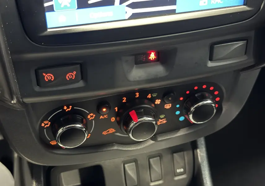 Gros plan sur les commandes de climatisation du Dacia Duster 2015, avec voyants orange et boutons rotatifs noirs.