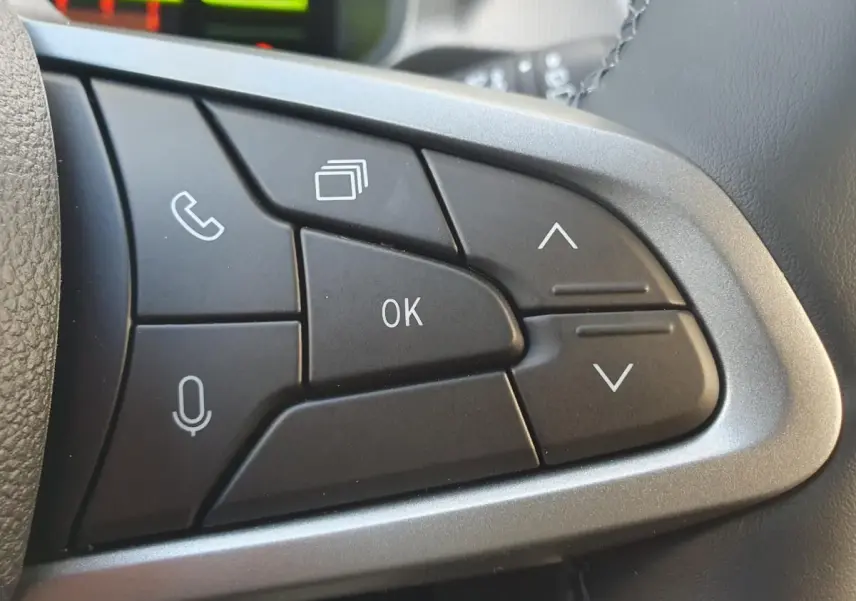 Gros plan sur les commandes multifonctions noires du volant du Dacia Duster 2026, finition métal brossé.