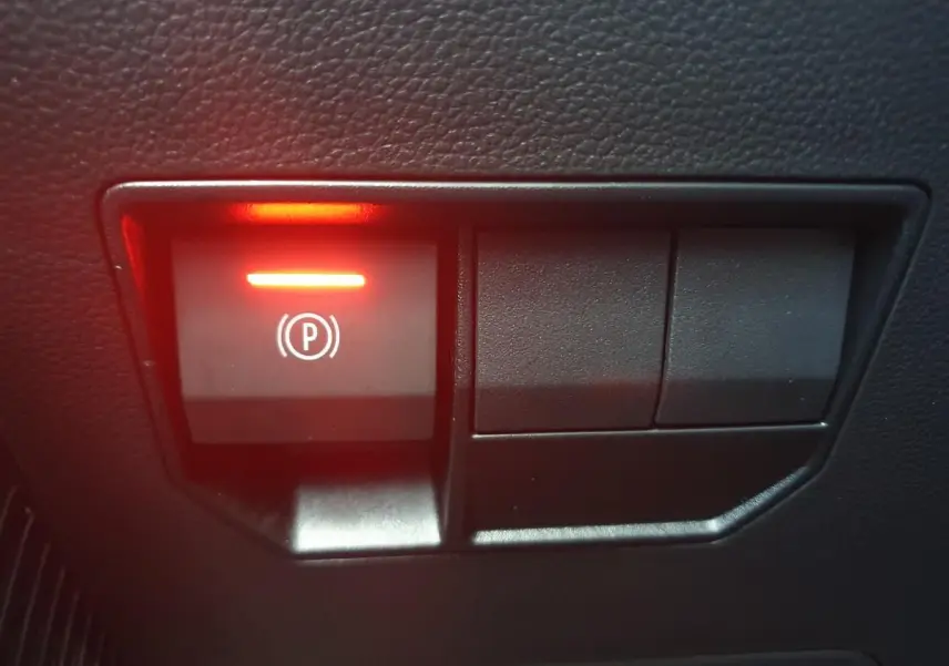 Gros plan sur le bouton de frein de stationnement électrique allumé, intérieur noir du Dacia Duster 2026.