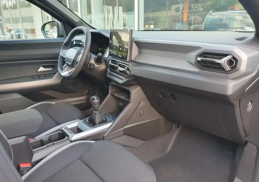 Vue intérieure côté passager du Dacia Duster 2026, montrant la console centrale avec boîte manuelle et écran tactile.