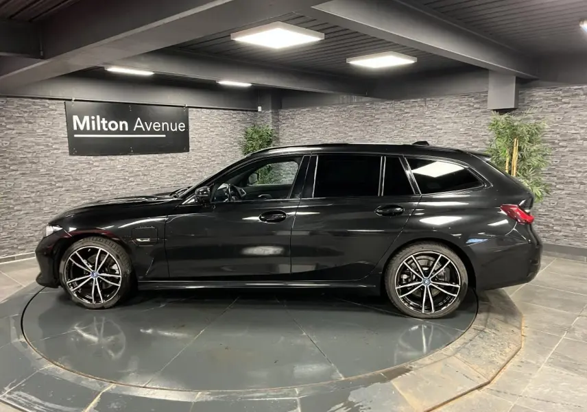 BMW Série 3 320e Touring noire vue de profil côté gauche avec jantes 19 pouces bicolores en intérieur showroom.