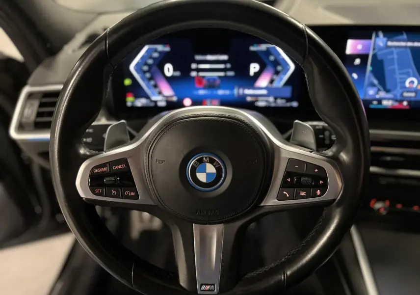 Vue rapprochée du volant M en cuir noir avec commandes intégrées et tableau de bord numérique lumineux d'une BMW Série 3 Touring.