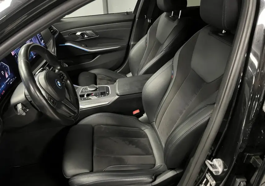 Vue intérieure côté conducteur de la BMW Série 3 320e Touring noire, sièges sport M en cuir et alcantara avec surpiqûres bleues.