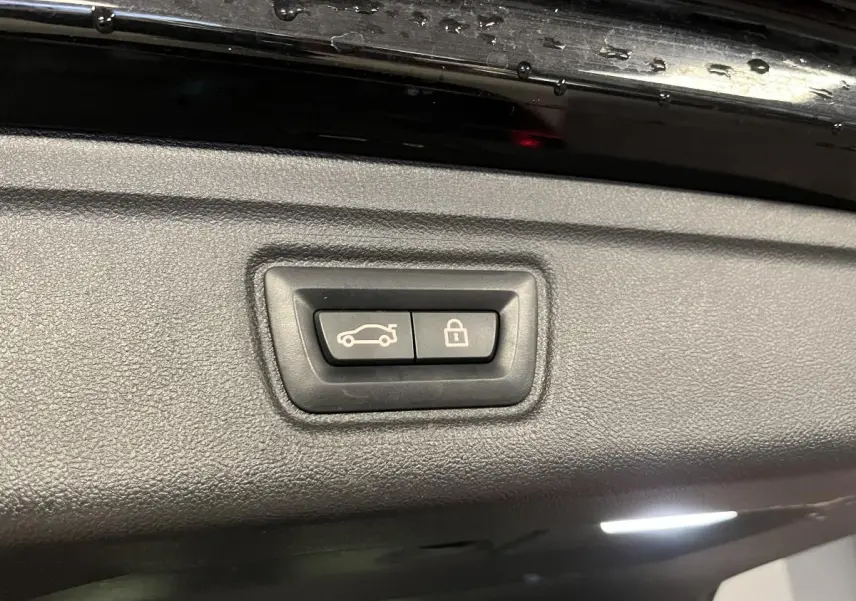 Gros plan sur les boutons d’ouverture et de verrouillage du coffre d’une BMW Série 3 Touring noire, vue intérieure du hayon.