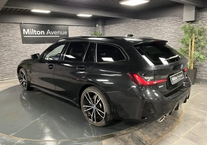 BMW Série 3 320e Touring noire vue 3/4 arrière droit, jantes M sport 19 pouces et double sortie d’échappement.