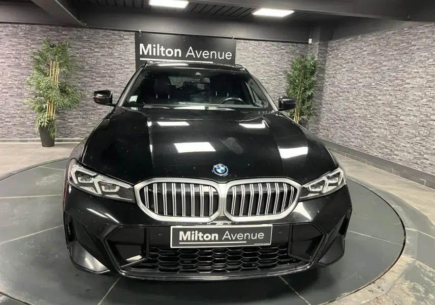 Vue avant d'une BMW Série 3 G21 320e Touring noire avec calandre double haricot et phares LED, en showroom.