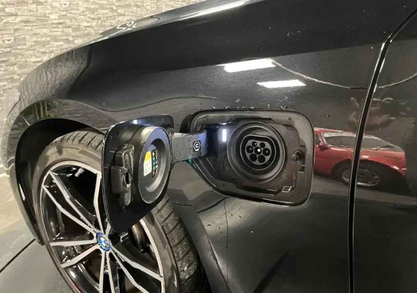Prise de recharge ouverte côté gauche arrière d’une BMW Série 3 Touring 320e noire avec jante 19 pouces bicolore.