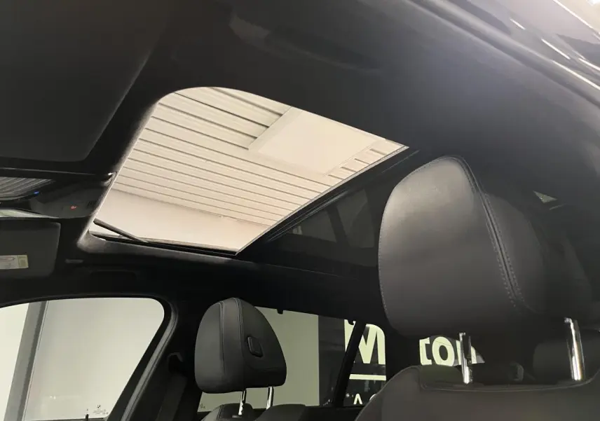 Vue intérieure du toit ouvrant panoramique en verre et des appuis-tête avant en cuir noir d'une BMW Série 3 Touring noire.