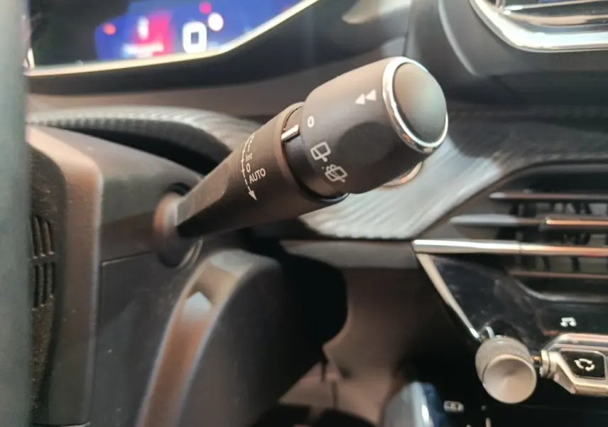 Gros plan sur la commande d’essuie-glace du tableau de bord noir de la Peugeot 208 blanche, version PureTech 100 S&S Allure Business.