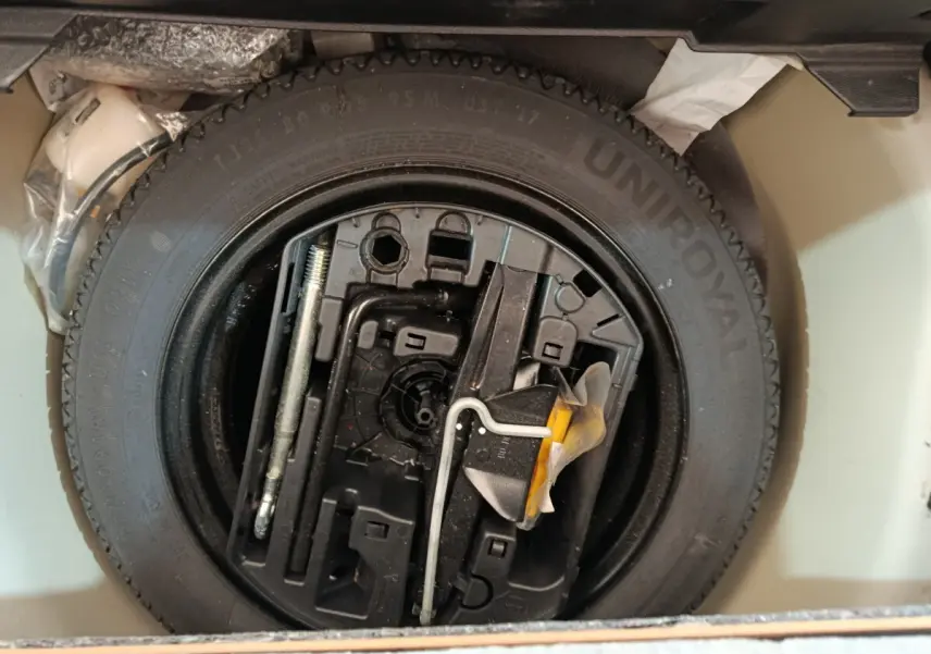 Vue rapprochée de la roue de secours noire et des outils de bord dans le coffre d'une Peugeot 208 blanche.