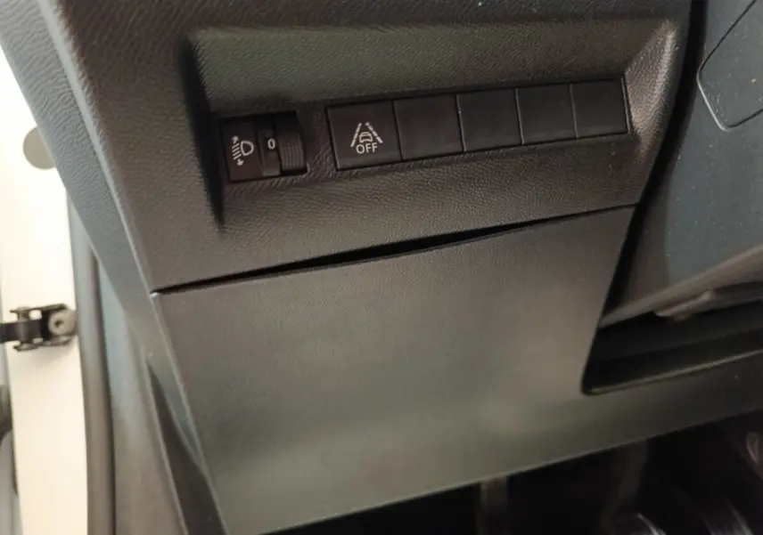 Détail du tableau de bord côté gauche d’un Peugeot 208 blanc, avec commandes de réglage des phares et d’aide au maintien de voie.
